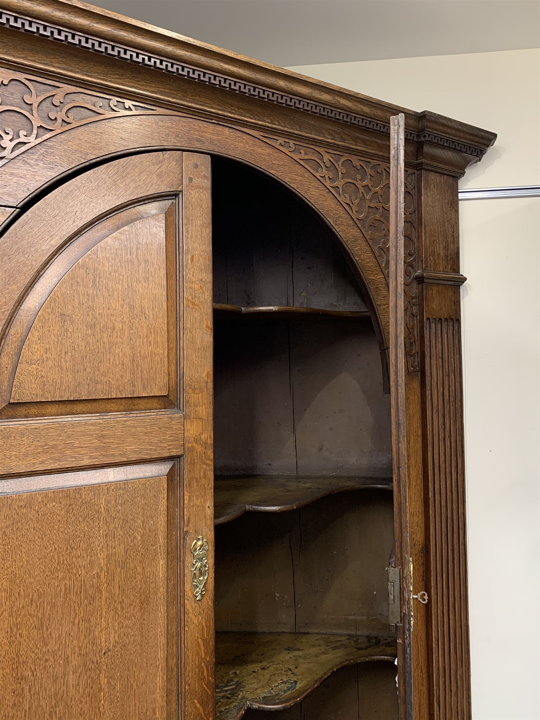 Large George III oak corner cupboard, projecting cornice over two stepped arch doors with fielded panels and blind fret work spandrels, flanked by fluted uprights, cupboard below enclosed by two fielded panel doors, the painted interior fitted with shaped shelves
 