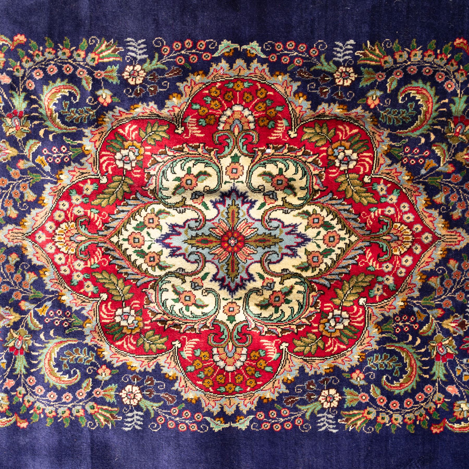 Persian Kashan rug, deep blue ground with central red and ivory lobed medallion framed by dense floral motifs, multiple borders with foliate and geometric design in red, blue and ivory, from the central Iran region