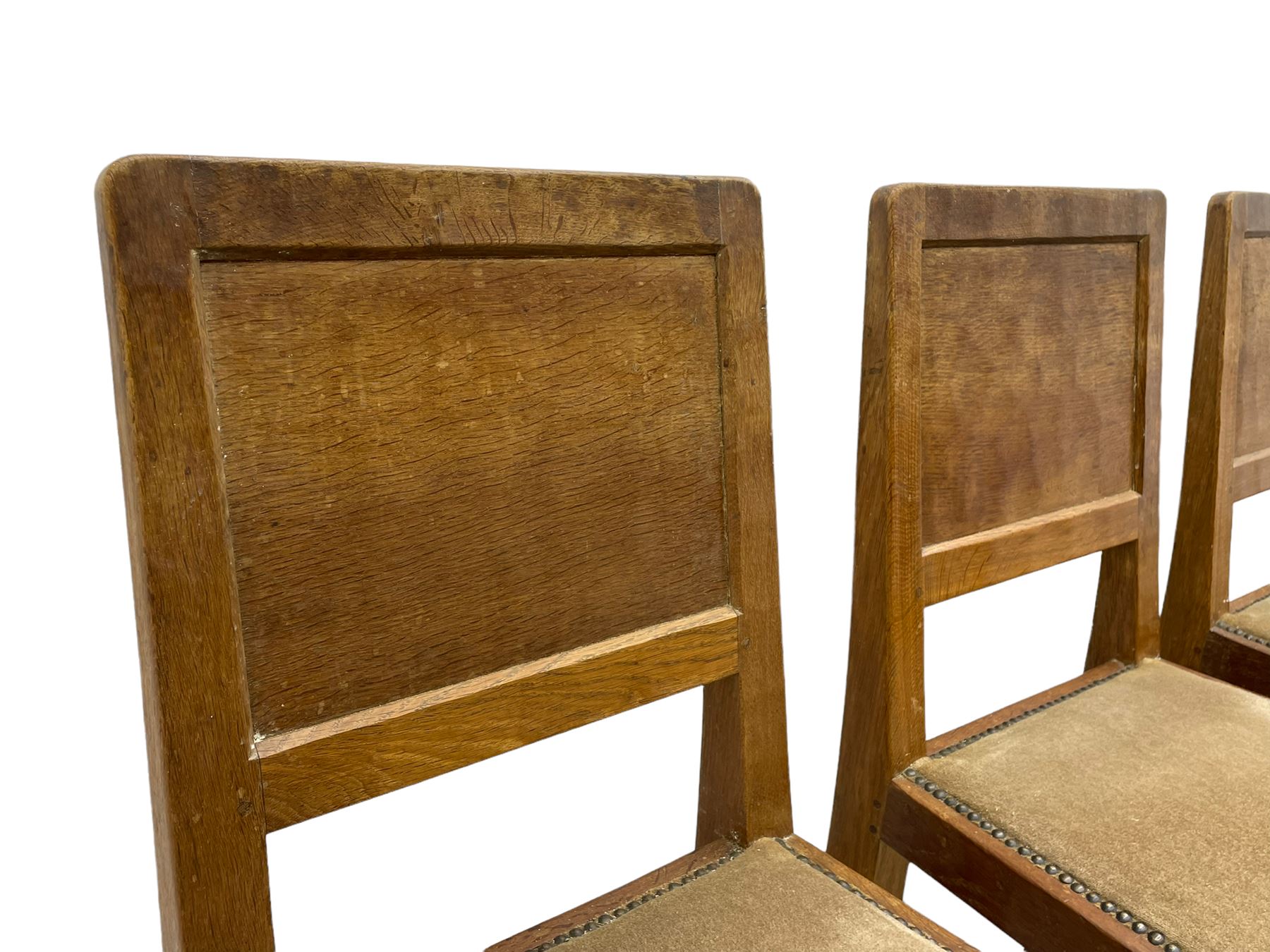 'Eagleman' set four oak dining chairs, adzed panelled backs, upholstered seats with stud work band, the side rails relief carved with inset eagle signature, shaped octagonal supports joined by stretchers, by Albert Jeffray of Sessay, Thirsk