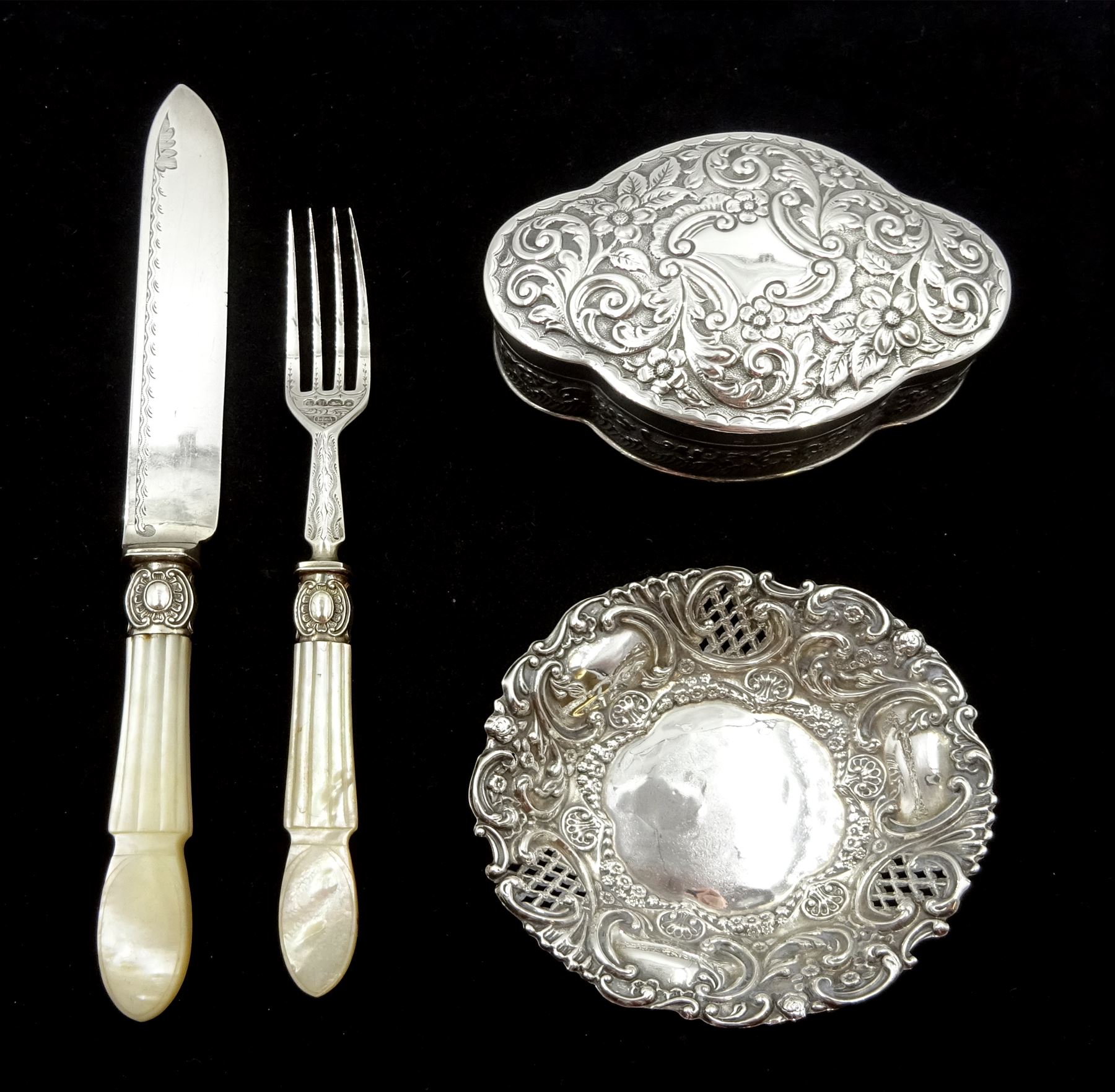 Victorian silver lidded trinket box, with embossed decoration by John Edward Wilmot, Birmingham 1900, silver bladed knife and fork with mother of pearl handles by Atkin Brothers, Sheffield 1862 and an embossed silver dish hallmarked (4)