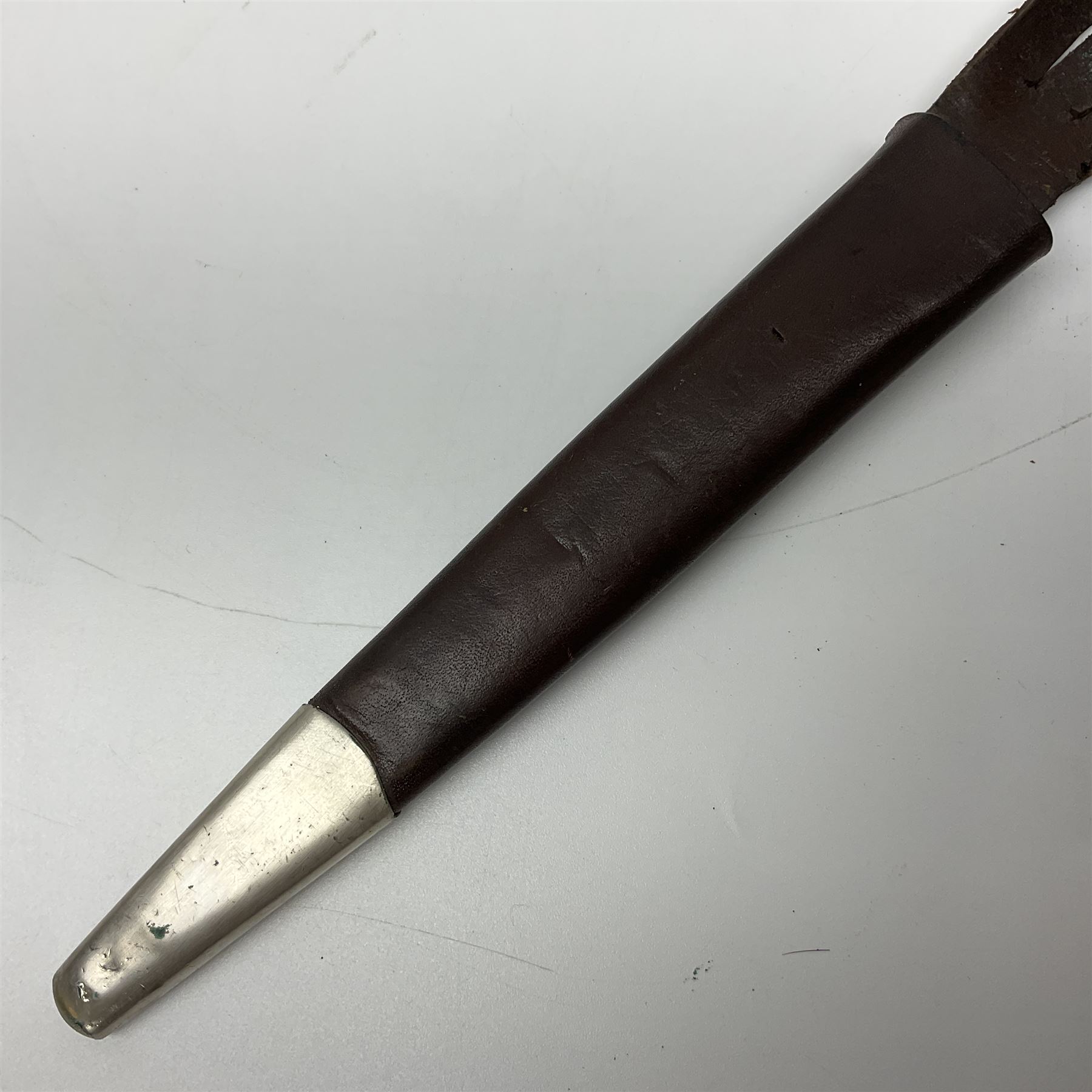 First Pattern Fairburn Sykes ''F-S'' Fighting Knife by Wilkinson Sword Ltd., the 17cm double edge steel blade with raised medial ridge to each side, each side of the ricasso with a recessed panel, one side with maker's name, the opposing side etched THE F~S FIGHTING KNIFE, with nickel plated brass recurving crossguard and diamond cut grip; in leather scabbard with metal chape