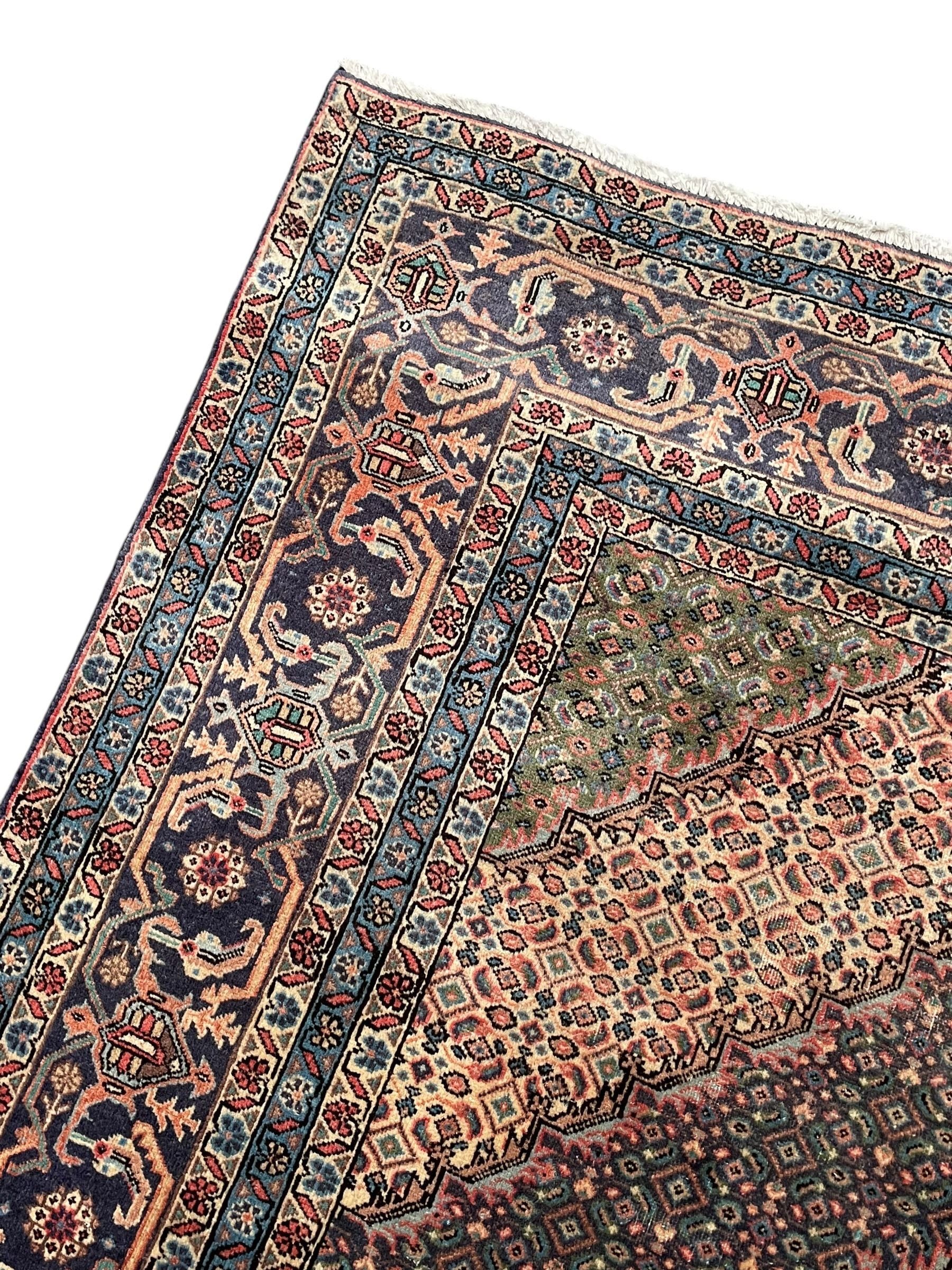 Persian Bidjar peach ground carpet, central pole medallion enclosed within lozenge field and spandrels, decorated all over with small Heratti motifs, the main border with trailing pattern decorated with stylised plant and Boteh motifs, within two triple band guard stripes with repeating flower head decoration 