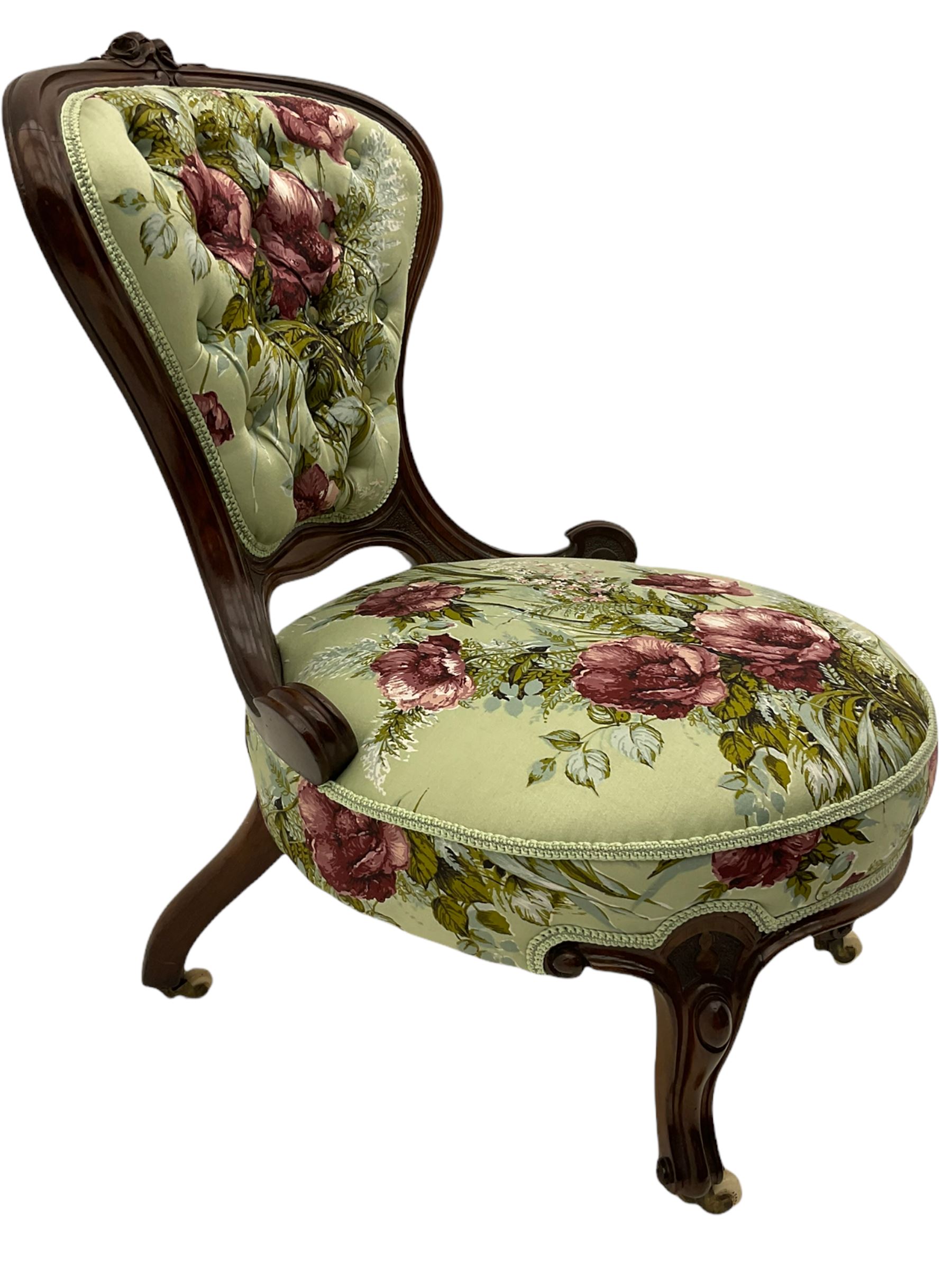 Victorian walnut framed nursing chair, spade shaped back carved with flower heads, upholstered in buttoned rose patterned fabric, on scroll carved cabriole supports terminating at brass and ceramic castors