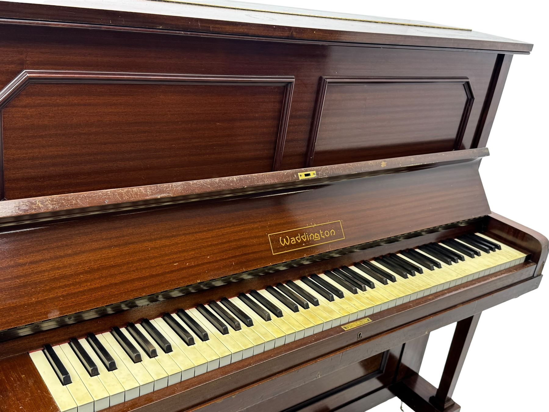 Waddington - Edwardian mahogany upright piano, rectangular top with panelled front, rounded key cover, makers name on fallboard, raised on bracket supports with castors