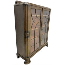 Early 20th century oak bookcase or display cabinet, raised back with carved floral decoration, fitted with two astragal glazed doors enclosing three adjustable shelves, on scroll feet