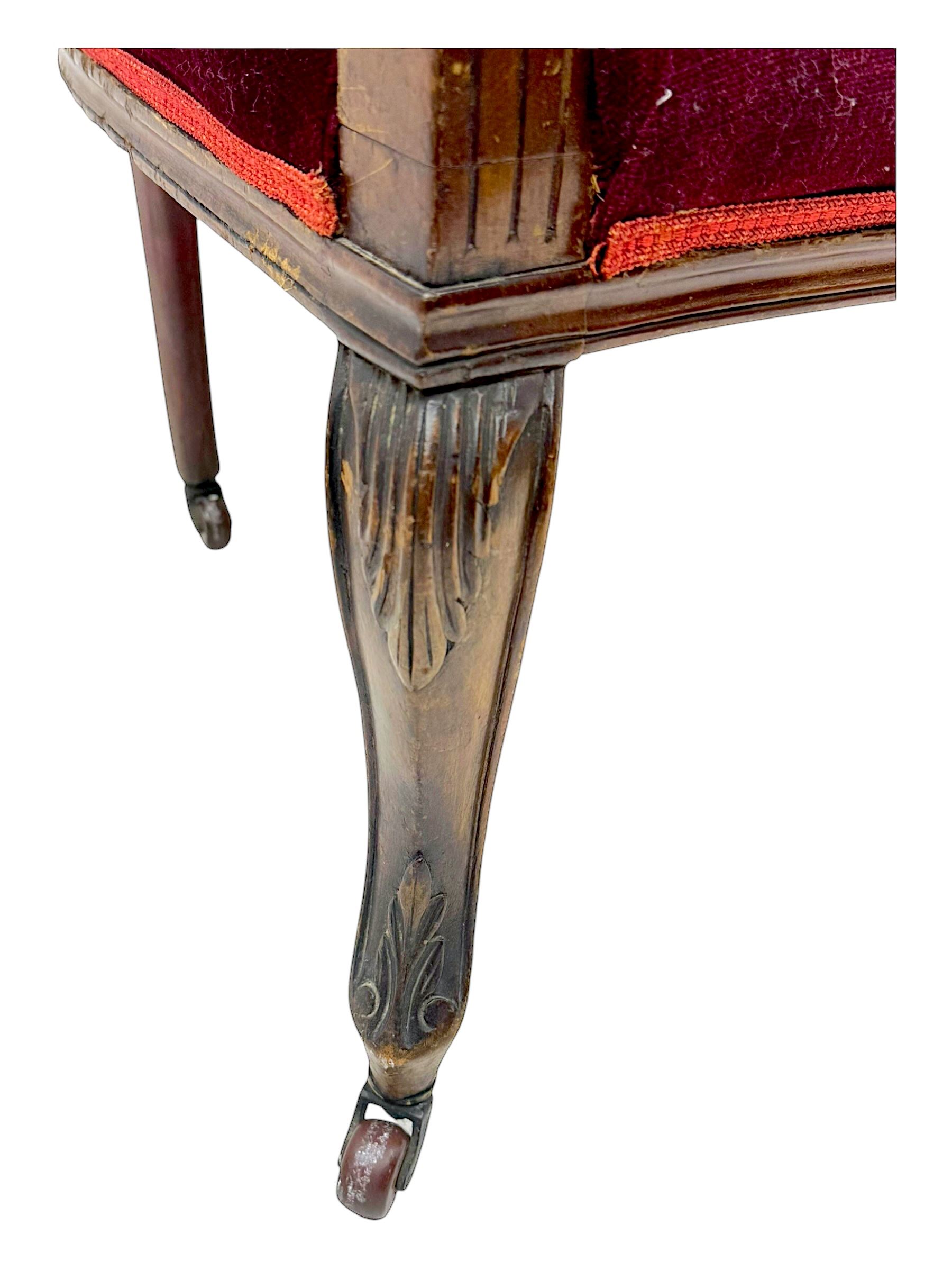 Late Victorian stained beech framed sofa, the backrests, seat and padded arms upholstered in deep red fabric, carved crest rail with scroll and foliate motifs supported by carved uprights, on cabriole supports with leaf carvings terminating in castors