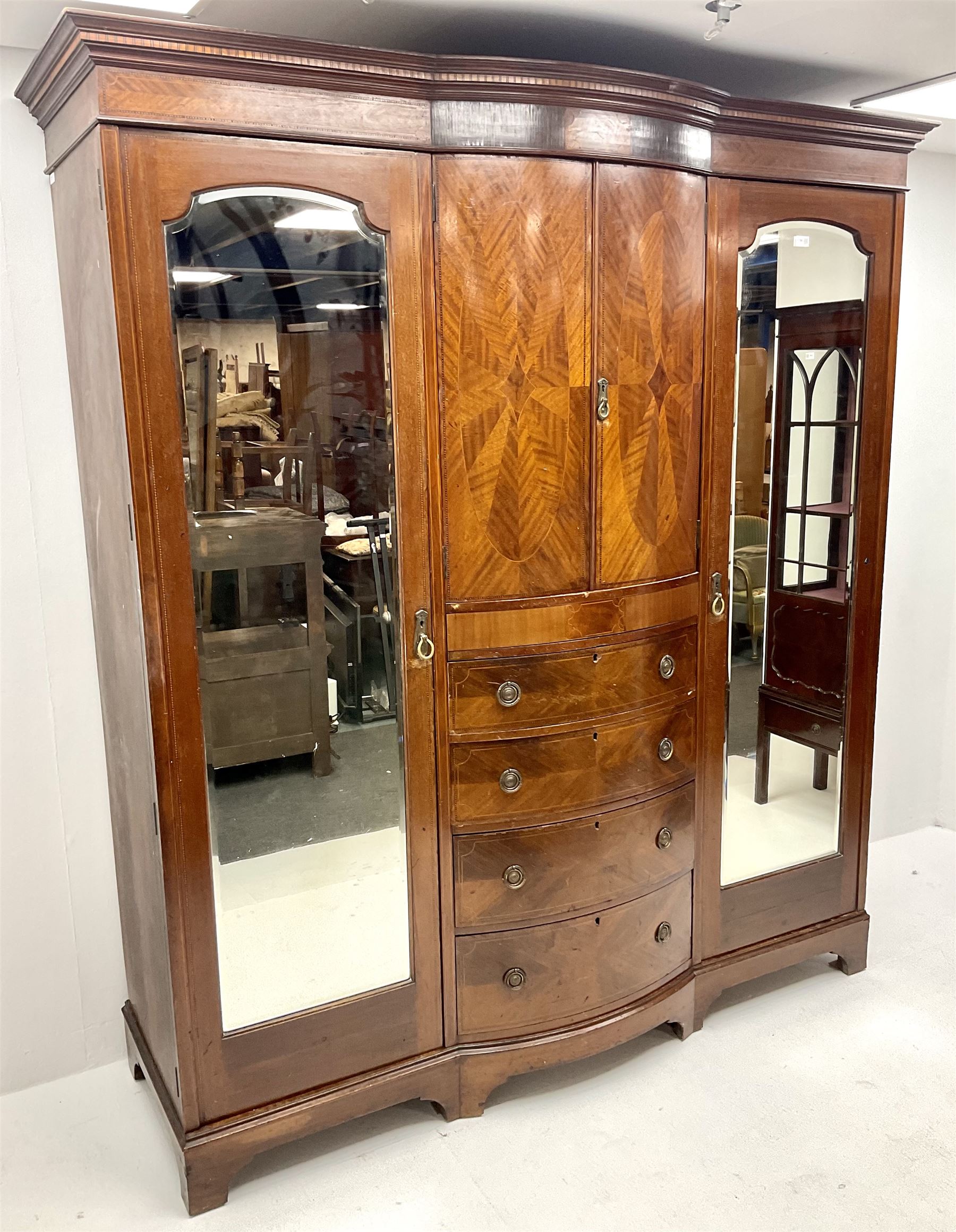 Edwardian inlaid mahogany triple wardrobe, bow front centre with two cupboards above four graduating drawers flanked by two bevel edged mirror doors, shaped platform base 