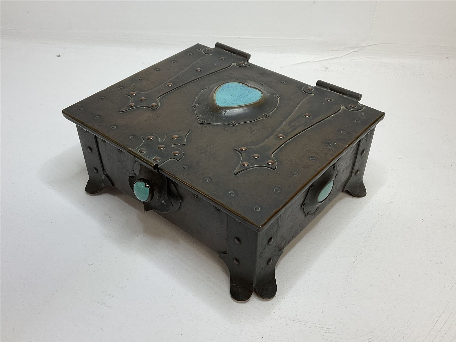 Arts and Crafts copper box, the lid decorated with stylised riveted hinges and inset with Ruskin type ceramic turquoise heart-shaped cabochon, the mount etched M.B 1913, and further cabochon roundel to each side panel, including one inset to the clasp acting as the knob to the locking mechanism, marked RS Douglas 1913 beneath, W16.5cm H7cm D15cm