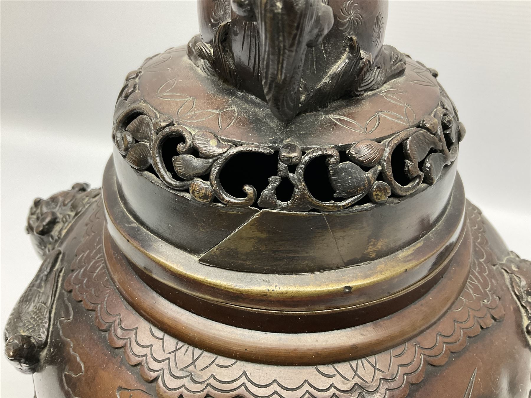 Japanese bronzed koro, the body of globular form with twin cast zoomorphic mask handles, decorated in relief with birds upon blossoming branches, against a ground incised with rushes and peonies, the flat toped domed cover with pierced band and surmounted by a cast figure of a Foo dog, the whole upon three zoomorphic mask feet, with impressed character type mark beneath, H35.5cm