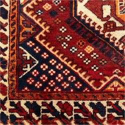 South West Persian Cori hand-knotted rug, red field with three central stepped lozenge medallions enclosing stylized geometric motifs surrounded by scattered rosette devices and angular ornaments within multiple geometric borders, with fringe ends  