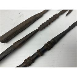 Native hand forged iron fishing spear, the V-shaped head with barbed neck and hewn haft L171cm; and two other hand forged iron spear heads, one with remains of copper bound haft (3)