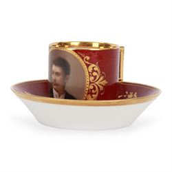 Late 19th century Vienna style coffee can and saucer, the cup with oval panel containing hand painted portrait of a gentleman, within a gilt foliate detailed surround, and upon a burgundy ground, the saucer with gilt band and sprigs upon a burgundy ground, with spurious shield mark beneath, cup H5cm saucer D12cm