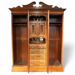Edwardian walnut triple combination wardrobe, projecting pediment with pierced foliate scroll cresting above a central cupboard flanked by bevelled mirrored doors, the central section with twin panelled cupboard doors carved with foliate scrolls, over open recess with mirrored back and turned supports, above two short and three long drawers with brass handles, interior fitted with hanging rails and shelf, raised on plinth base