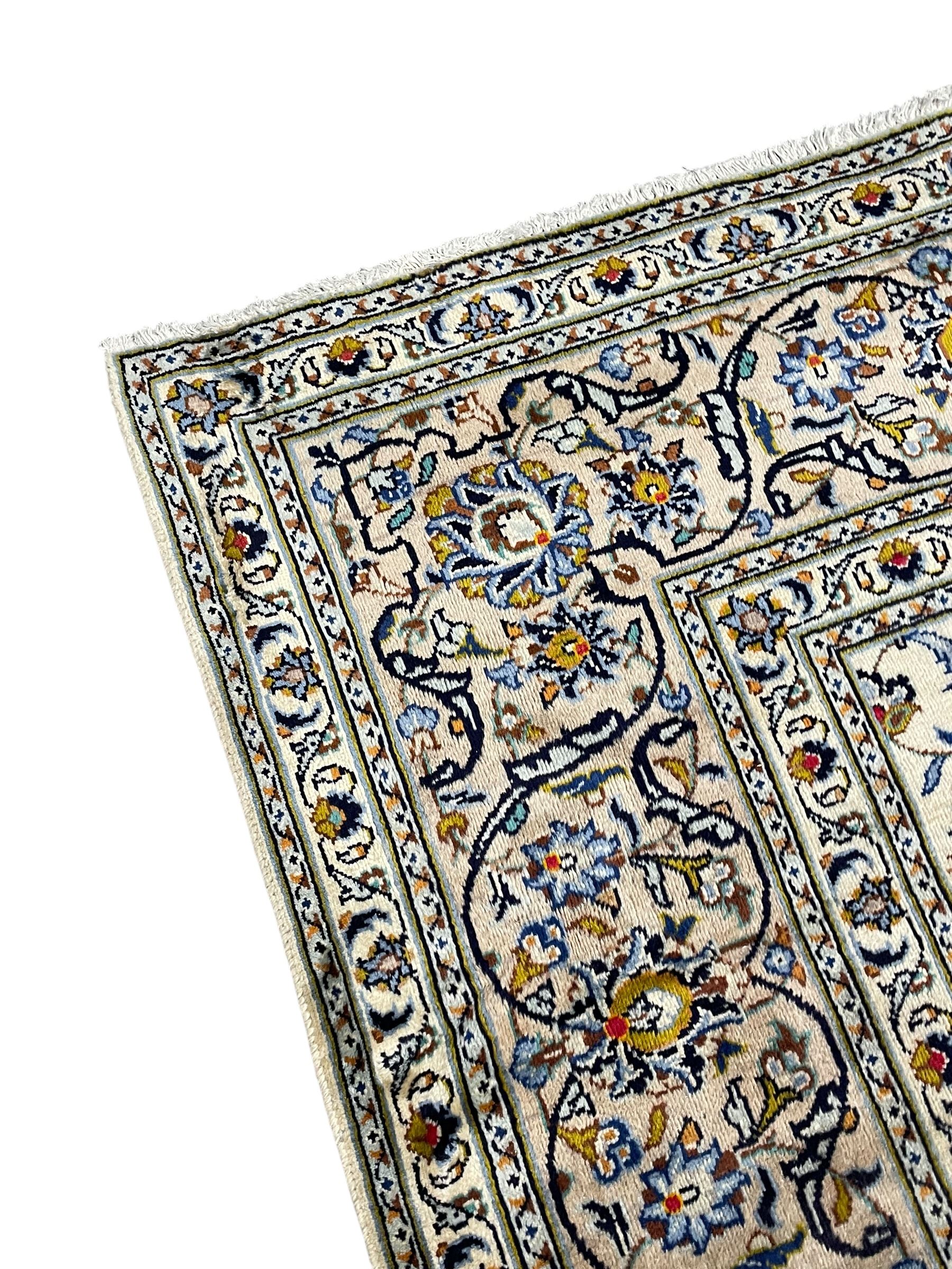 Persian Kashan Ivory ground carpet, the busy field decorated all over palmettes and trailing branches, scrolling border interspersed with stylised plant motifs, within guard stripes