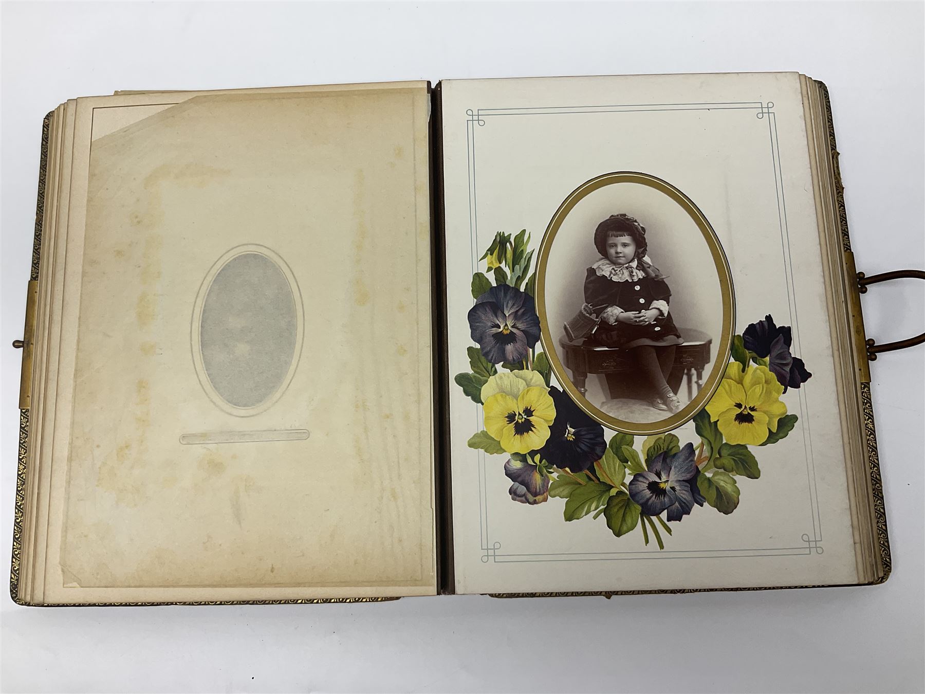  Victorian leather bound photo album, the interior leaves containing apertures of various sizes and shapes of portraits surrounded by printed floral designs, with brass clasp and painted gold decoration to edges, H30cm