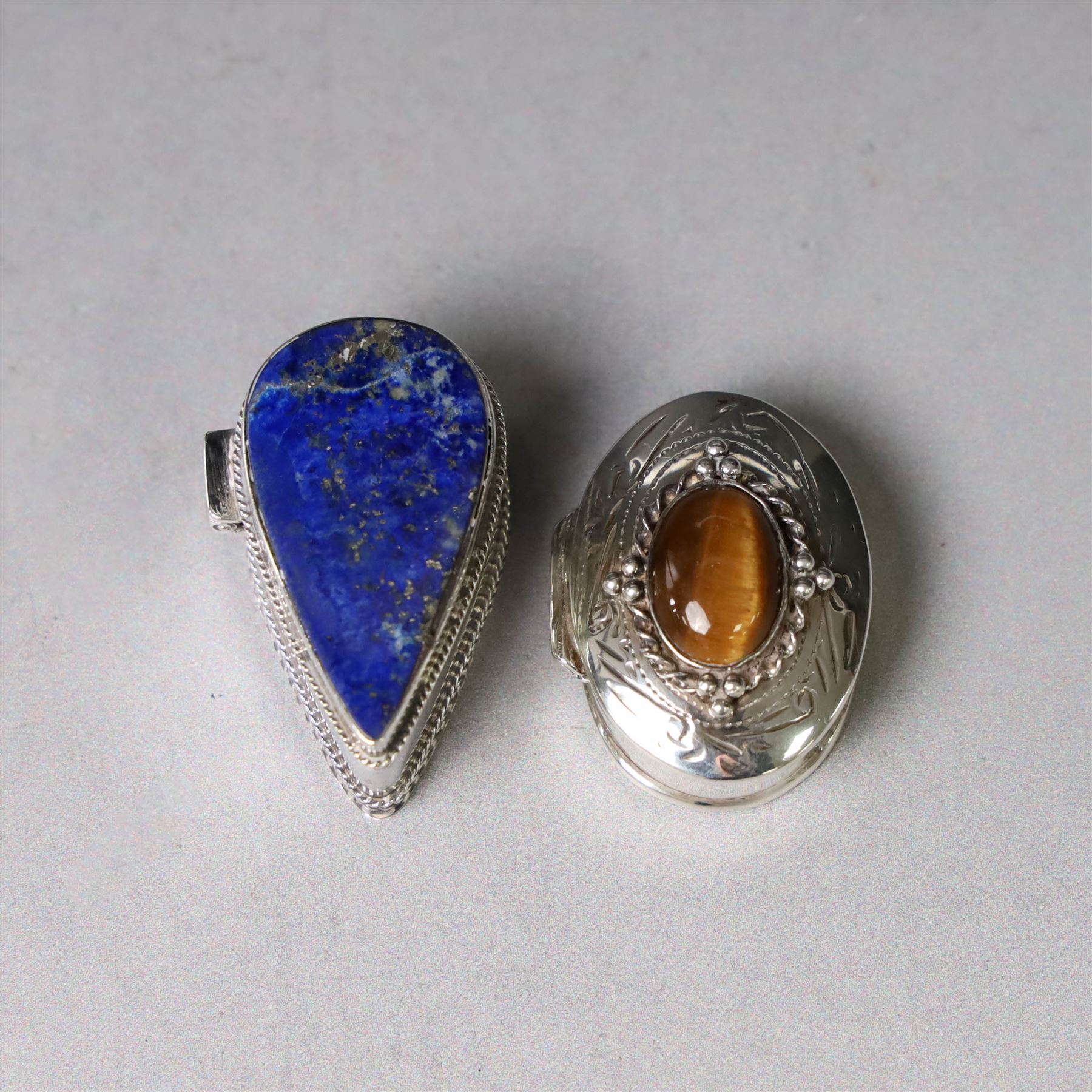 Two modern silver pill boxes, the first example of oval form, the hinged cover set with a tigers eye cabochon with beaded mount, and engraved scroll edge, hallmarked NC, London import 1995, W3cm, the second of teardrop form, the hinged cover set with lapis lazuli, marked 925, L3.5cm