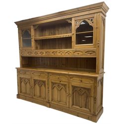 Ecclesiastical Gothic design waxed pine 8’ dresser, projecting cornice over two display cabinets, central shelf and ten small drawers, rectangular moulded top over four drawers and four cupboards, the doors with Gothic design arched panels carved with flower heads and foliage, on plinth base