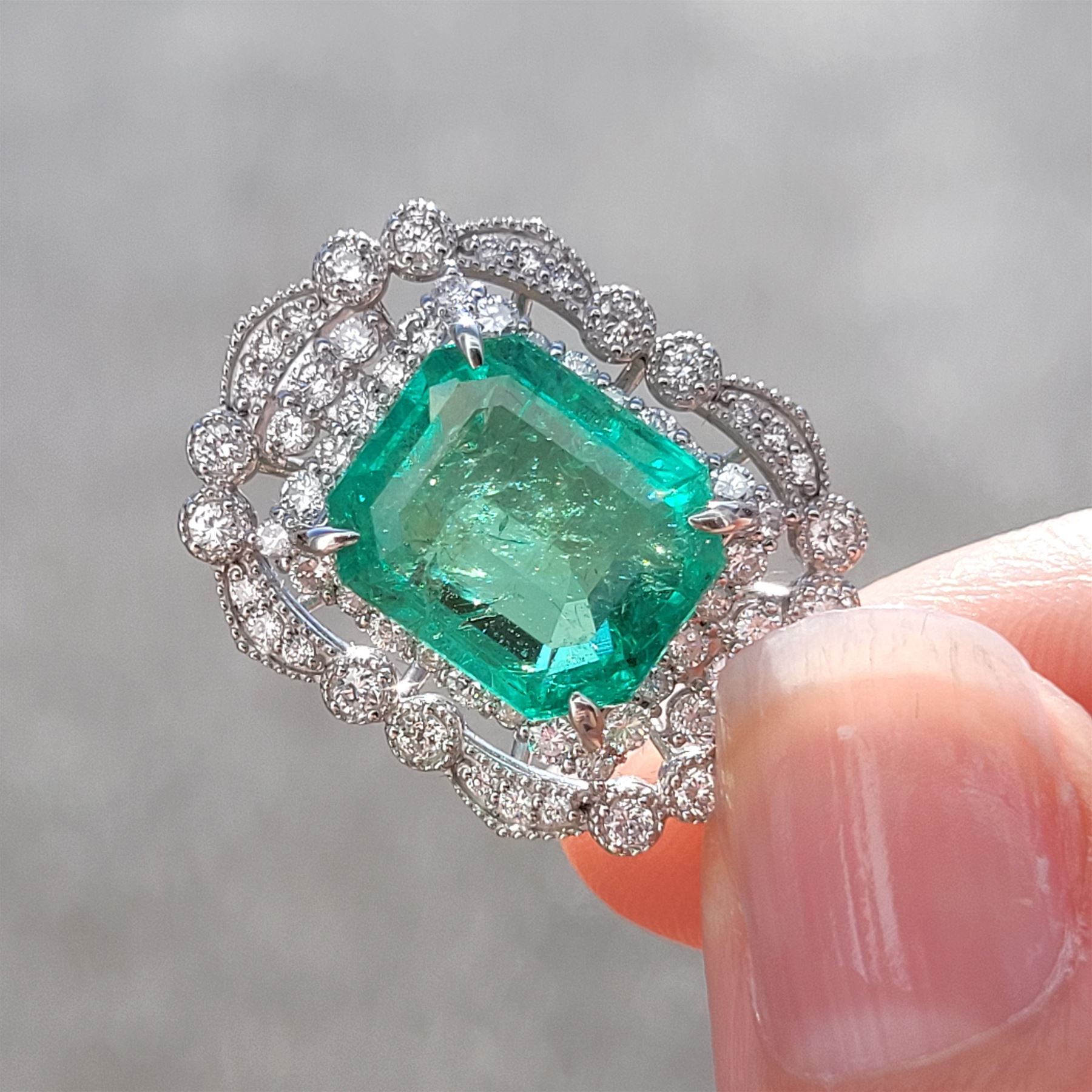 Platinum Colombian emerald and diamond pendant necklace, single octagonal cut emerald of 7.38 carat, surrounded by round cut diamonds in a fancy milgrain pierced design setting, stamped Pt 950, on a trace link chain necklace, total diamond weight 1.14 carat, with GCS certificate