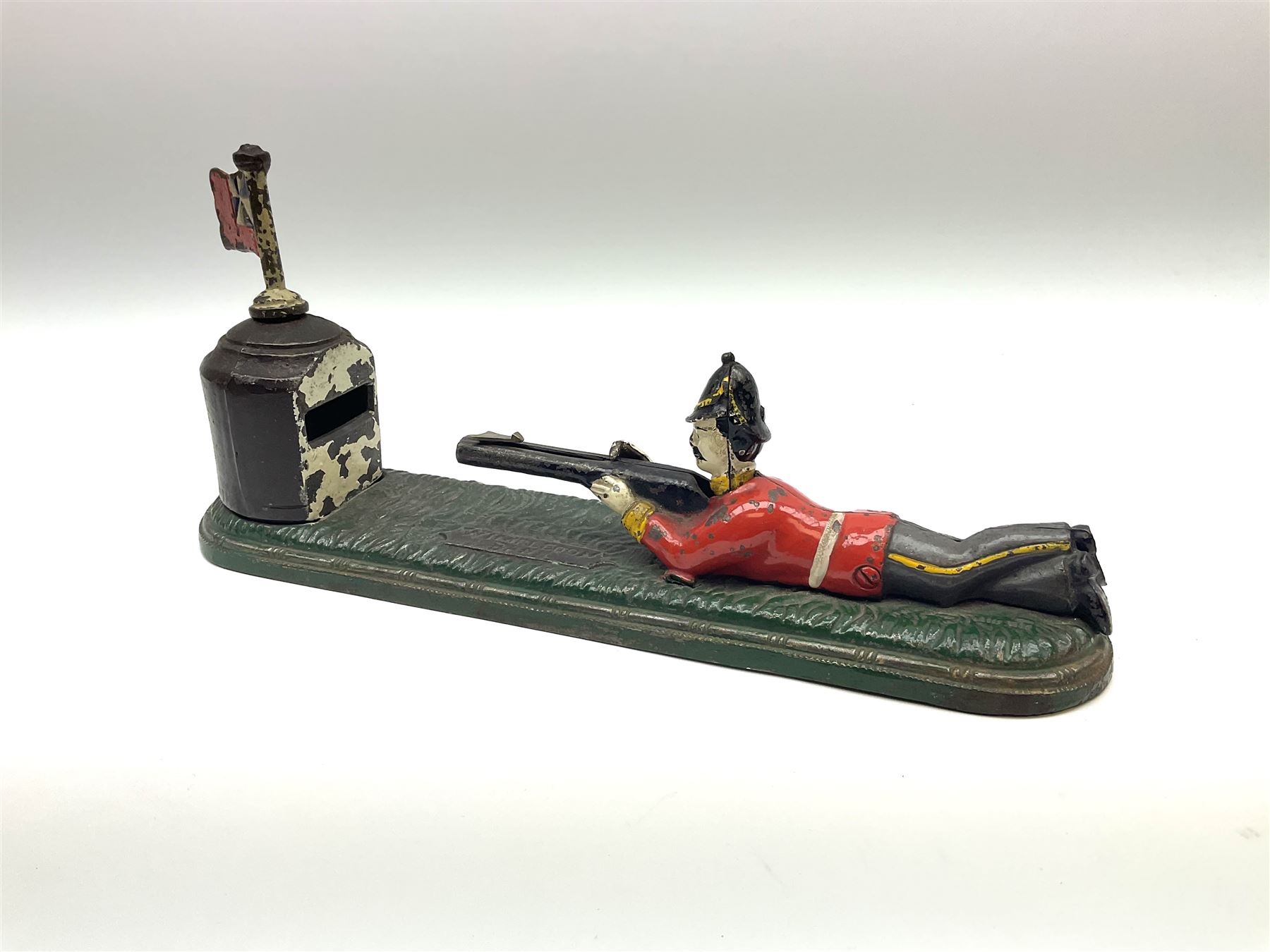 Very rare 19th century John Harper & Co. mechanical cast-iron money box, registered number 33821 patented 1885, inscribed on metal plaque 'Wimbledon Bank', based on the Queen's Trophy for shooting at Wimbledon, depicting a British Infantry man in red tunic and blue trousers lying on the ground using a gun to fire a brass coin launcher into a pill box with removable moving flag above L30cm