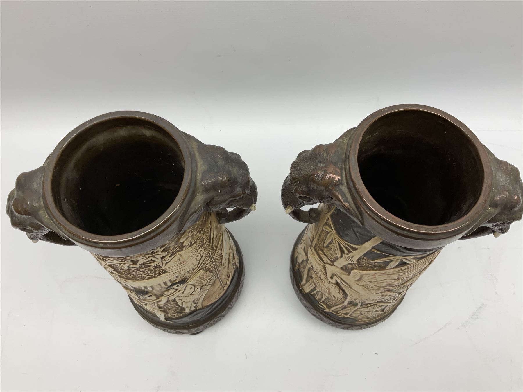 Pair of Bretby vases of tapering cylindrical form decorated with elephants, cranes and fishermen, the bodies with twin elephant mask handles, with coppered borders, raised upon three bun feet, stamped Bretby 2246 marks beneath, H32cm