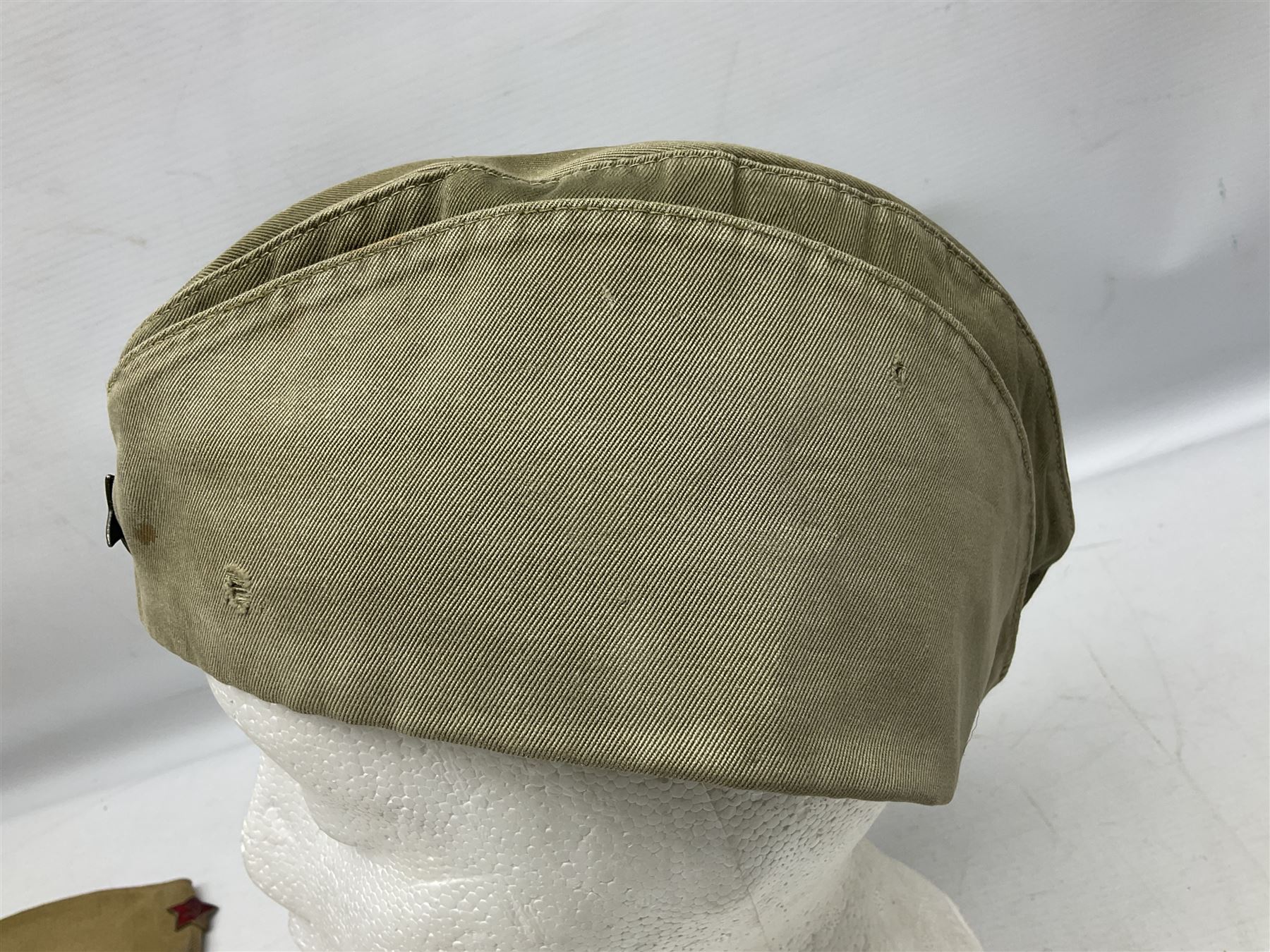 Four side caps - WW2 Russian, post-WW2 Russian and two East German; all with badges, one with multiple metal badges (4)