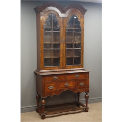  19th century Queen Anne style figured walnut twin arched cabinet on stand, two stepped glazed doors enclosing three shelves, above five drawers on turned supports and feet joined by shaped stretchers, W104cm, H218cm, D43cm  
