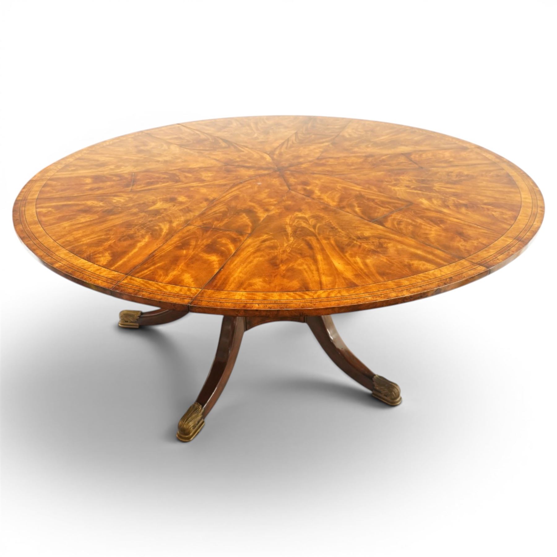 Theodore Alexander - Regency Revival figured mahogany 'Althorp Patent Jupe' extending dining table, the segmented circular top formed of six pull-out triangular divisions with inset fold-out leaves, raised on a large turned vasiform pedestal on a pentagonal platform base with ebonised stringing, terminating to five splayed supports with gilt metal acanthus scrolled feet, retailed by David Hick Interiors, Jersey