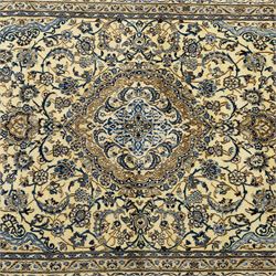 Central Persian Nain hand-knotted carpet, ivory ground, with silk highlights, centred by a shaped floral medallion with pendants, surrounded by scrolling foliate and floral motifs incorporating rosettes, palmettes and delicate vine work in blue, cream and beige tones, enclosed by blue spandrels and an ivory border with repeating palmettes and meandering vines, flanked by floral guard stripes, with cotton fringes