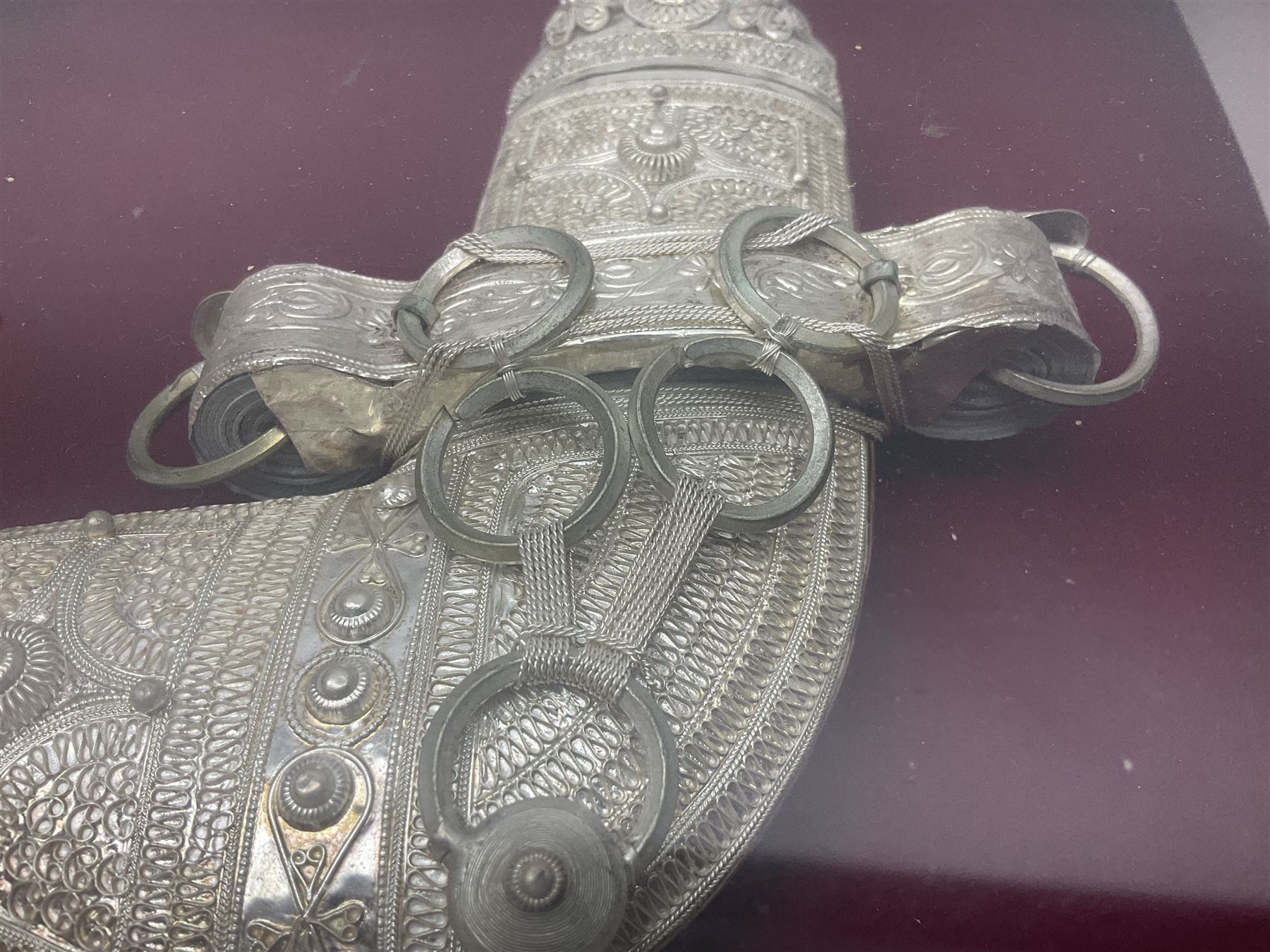 20th century silver Khanjar dagger from Oman, heavily decorated with filigree throughout, dome shaped pommel and waisted grip, the sheath with fastening rings, with miniature curved dagger accessory, housed in red lined glazed box frame, L38cm