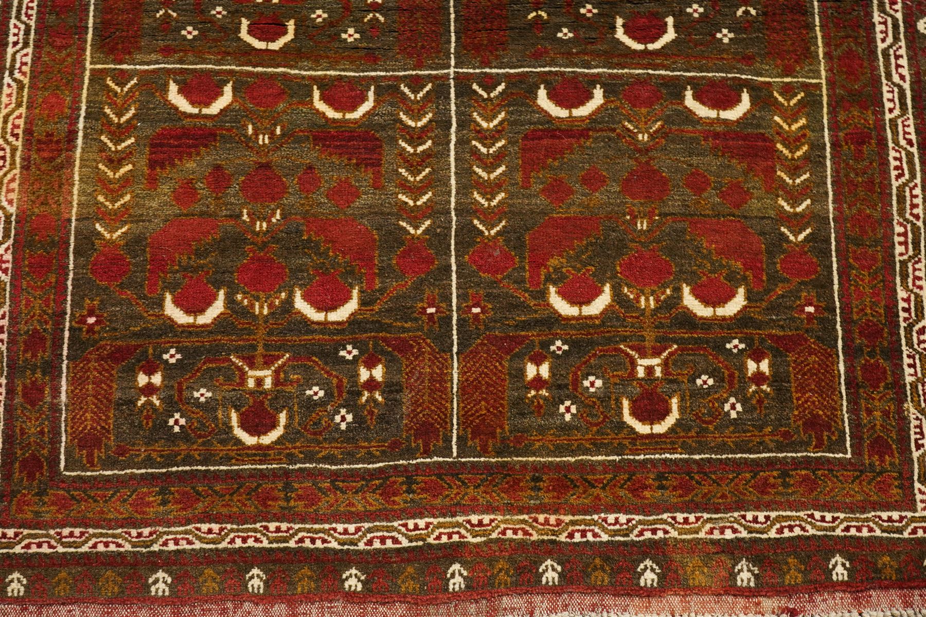 Baluchi hand-knotted prayer rug, dark brown ground divided into six panels decorated with stylised tree-of-life and flowering motifs in madder red and ivory, enclosed by multiple narrow geometric borders, with fringed ends