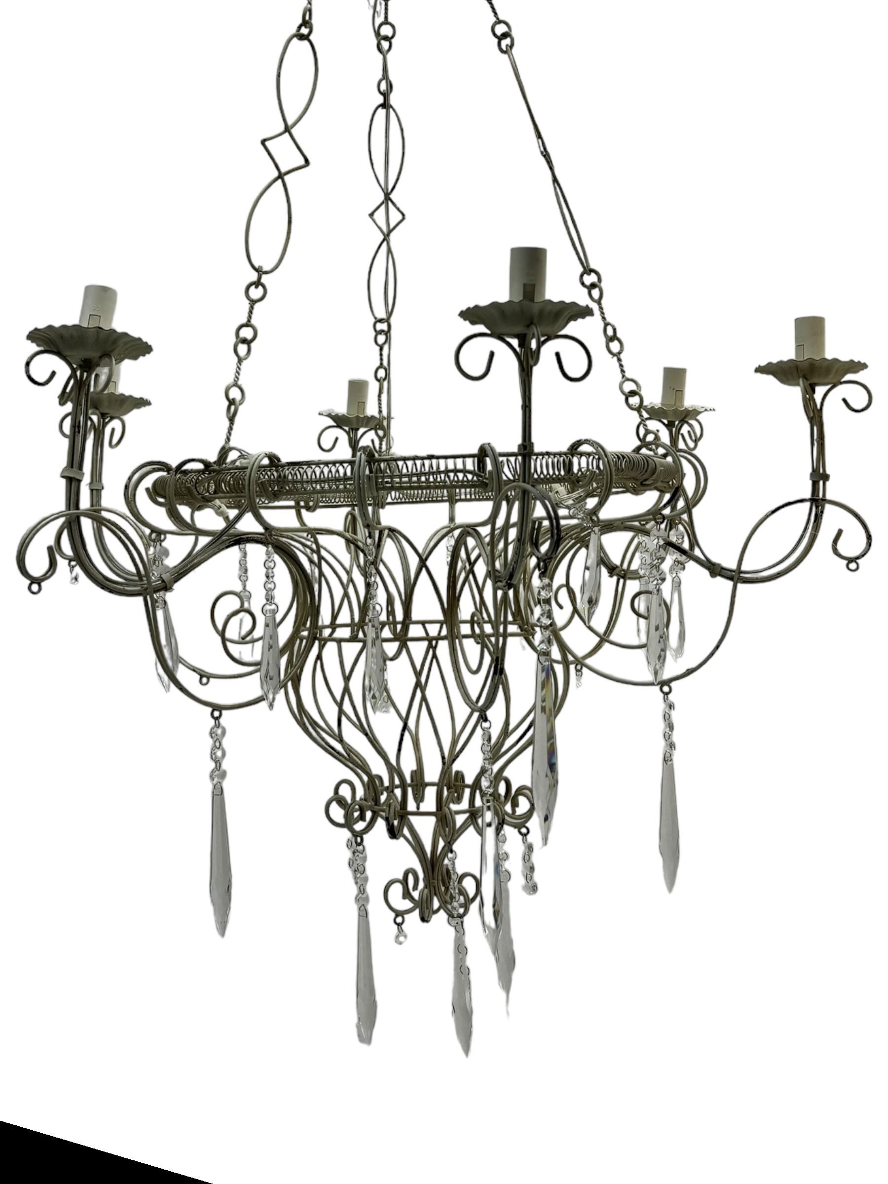 India Jane Interiors - six branch metal chandelier, the scrolled crown over circular bulbous body with six projecting branches, decorated with scroll work and glass pendants, in distressed white paint finish - ex-display/bankruptcy stock 