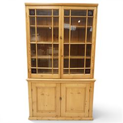 19th century pine glazed bookcase cupboard, twin astragal glazed doors with stained glass corner panels, enclosing fixed shelves, the lower section fitted with two panelled cupboard doors enclosing single shelf, on plinth base