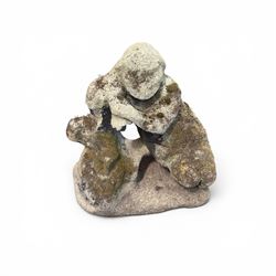 Carved composite stone garden figure, depicting a seated child with folded arms, weathered finish with moss and lichen growth, raised on an integral naturalistic base