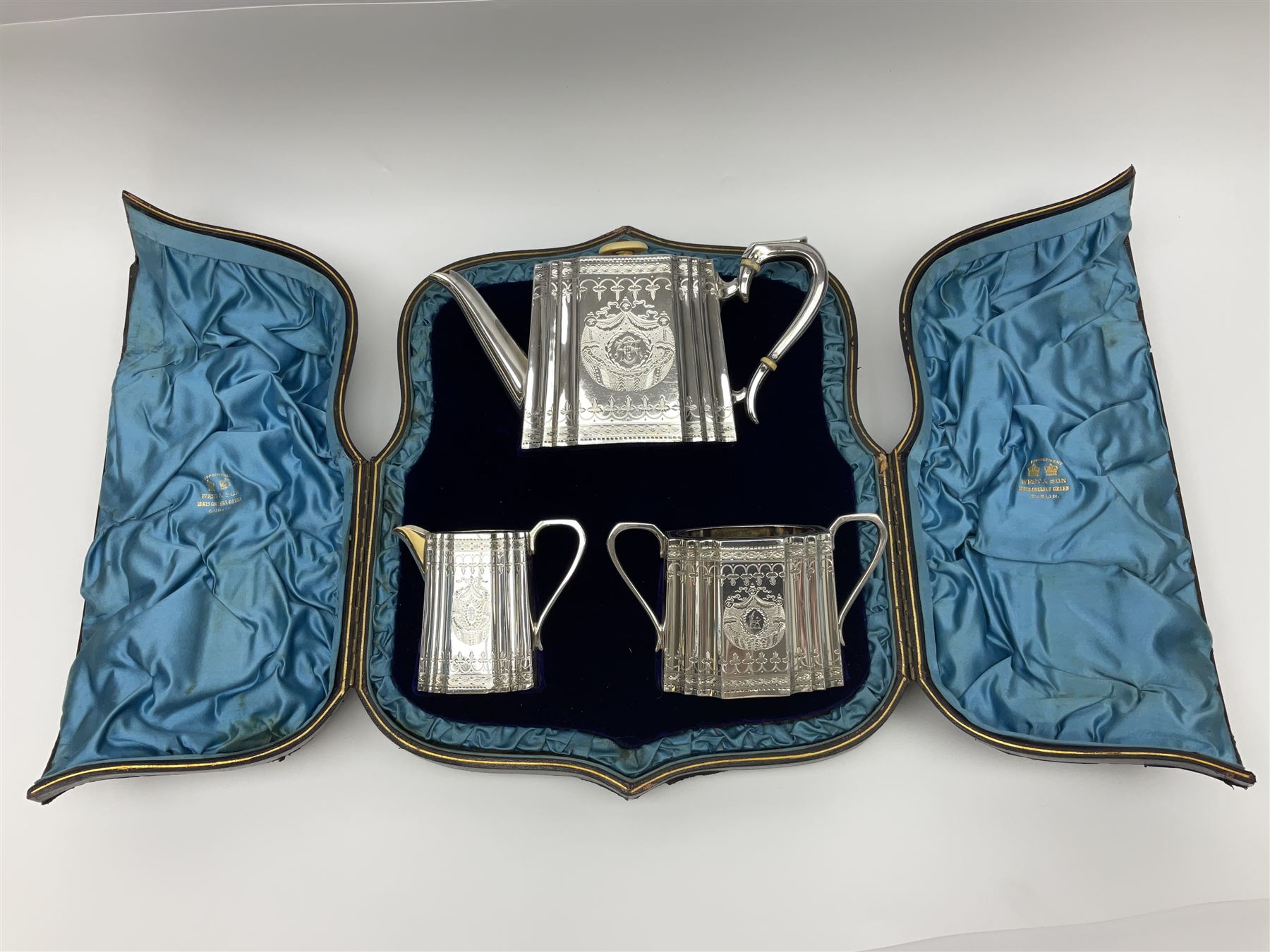 Victorian three-piece silver tea service, comprising teapot, twin handled open sucrier and milk jug, of oval form with shaped rim and C handles, each engraved with crests and bands of strapwork decoration, the milk jug and sucrier with gilt interiors, hallmarked Josiah Williams & Co, Exeter 1881, the teapot with ivory insulators and finial, all contained with a tooled leather, blue silk and velvet lined fitted case, retailed by West & Sun, Dublin 
This item has been registered for sale under Section 10 of the APHA Ivory Act