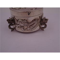 Late 19th/early 20th century Chinese export silver box, of circular form, the body and removable cover decorated in relief with circling dragons, upon three dragon head feet, stamped beneath with character mark, 90 and WH for Wang Hing, H6.5cm, D9cm
