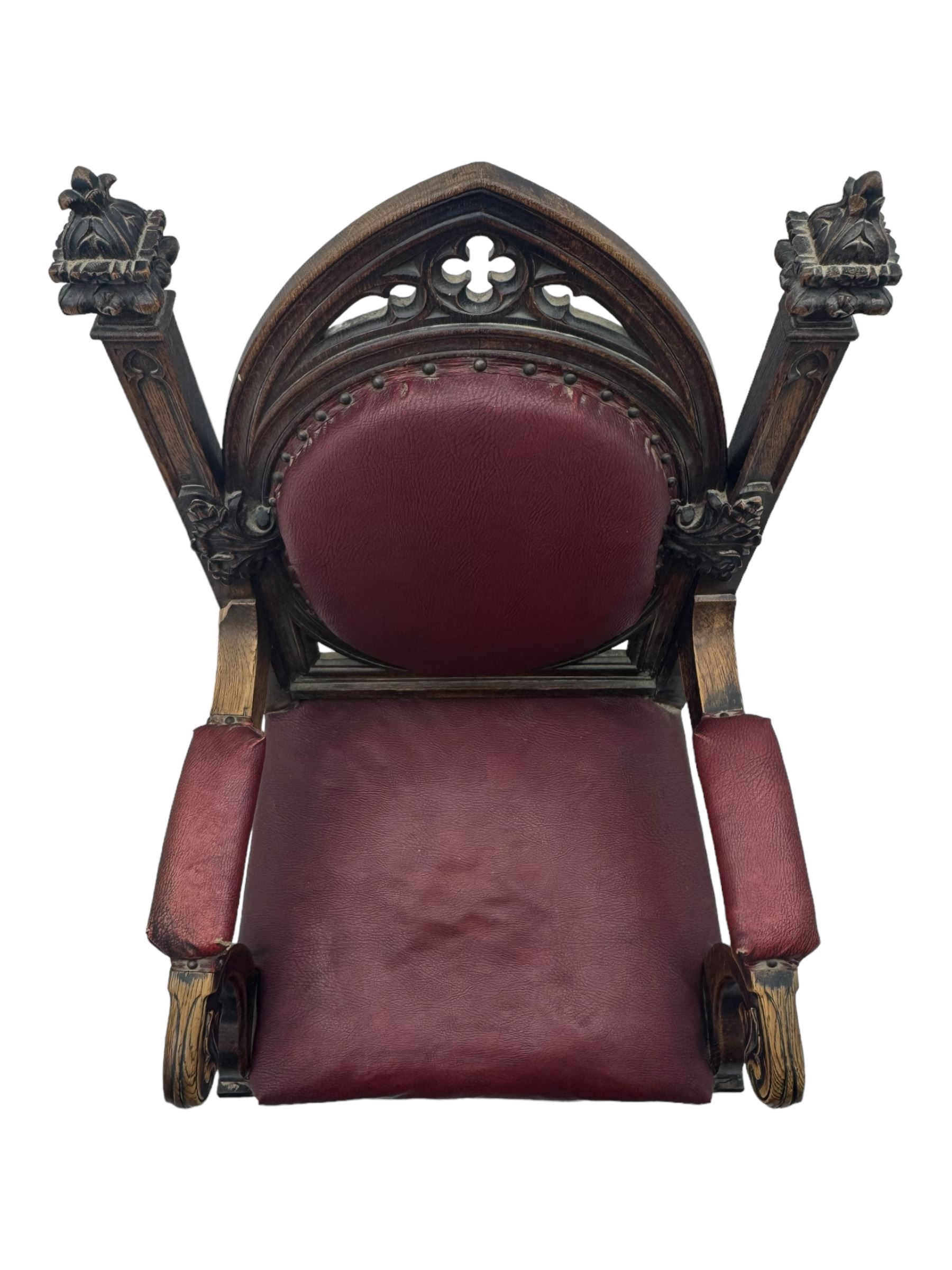 Late Victorian Gothic-revival armchair, arched crest rail carved with tracery and trefoil detail, padded circular back and seat, brass studded burgundy leather upholstery, shaped armrests with scrolled terminals, on square tapering supports