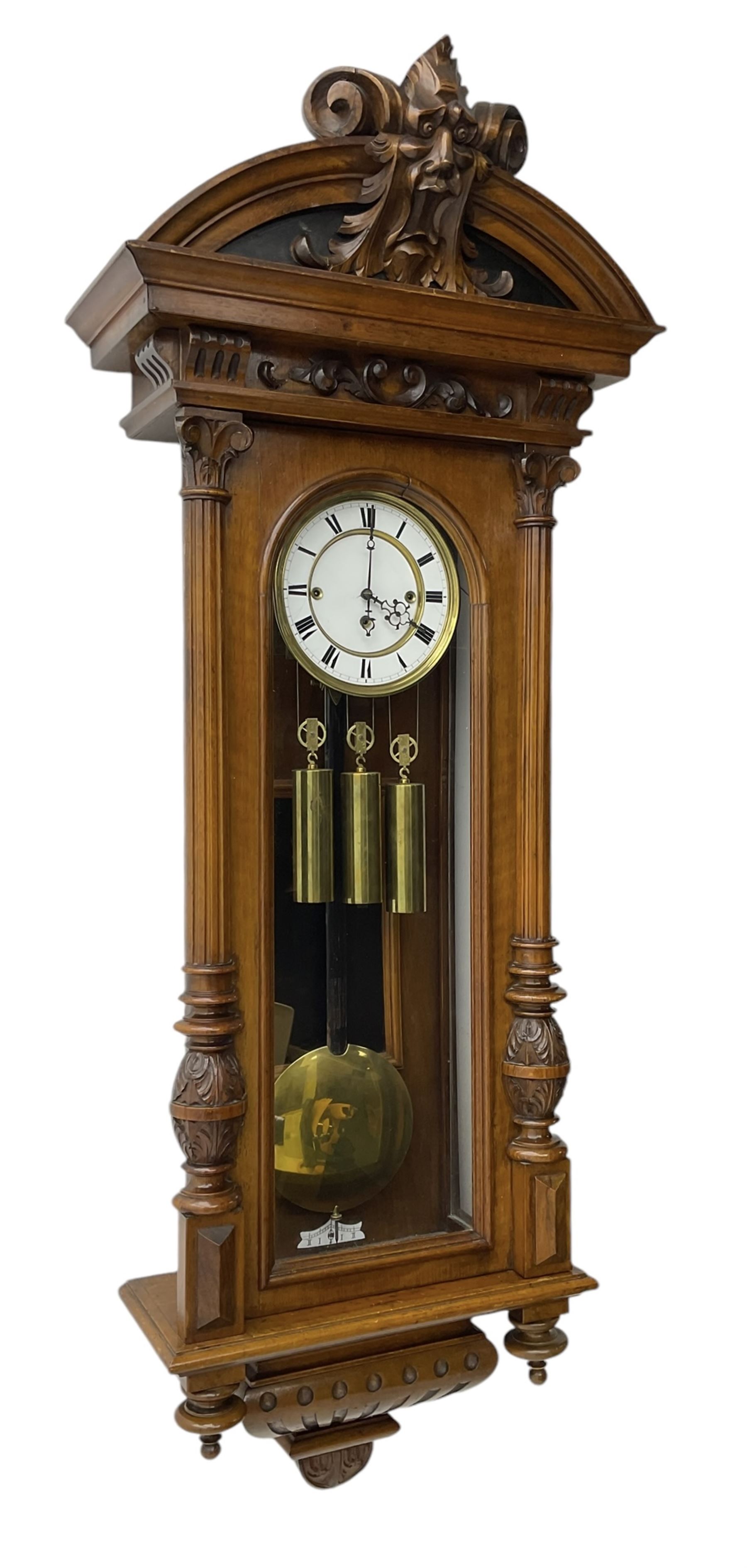 German- Late 19th century 8-day walnut cased Vienna regulator wall clock c1870,  with a broad arched pediment and heavily carved grotesque to the centre, carved frieze beneath with reeded columns to the front of the fully glazed door, carved ogee plinth and pendants to the base, two part enamel dial with Roman numerals and pierced steel hands, ebonised pendulum rod with a brass faced bob and beat plate, three matching brass cased weights and pulleys, grand sonnerie three train striking movement with a deadbeat escapement striking the quarters and hours on two coiled gongs. 
With repeat work.