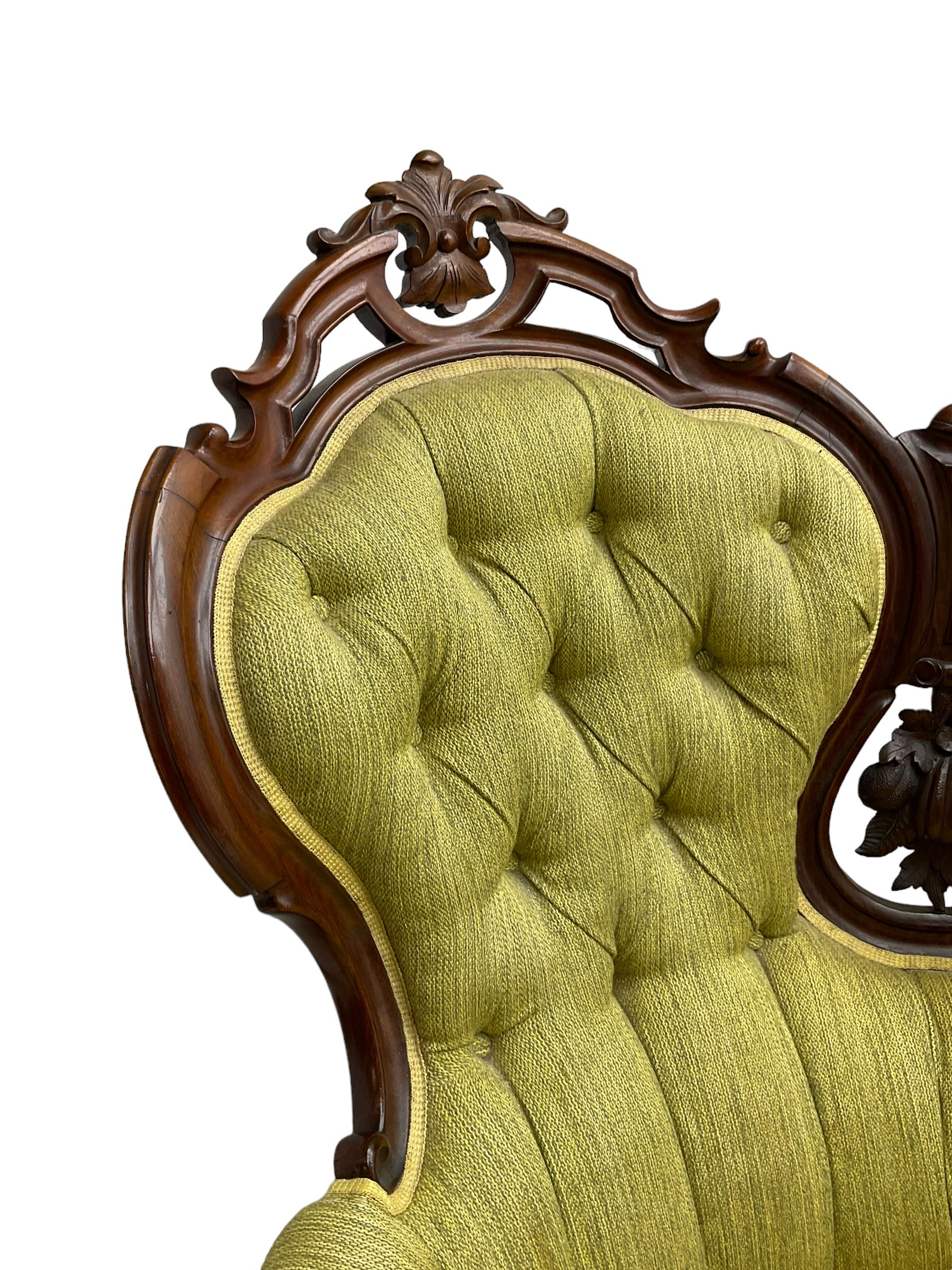Victorian walnut settee, triple back with pierced and scroll-carved cresting rails over carved fruit and foliage decoration, upholstered in buttoned green fabric, serpentine seat and carved apron, on cabriole feet