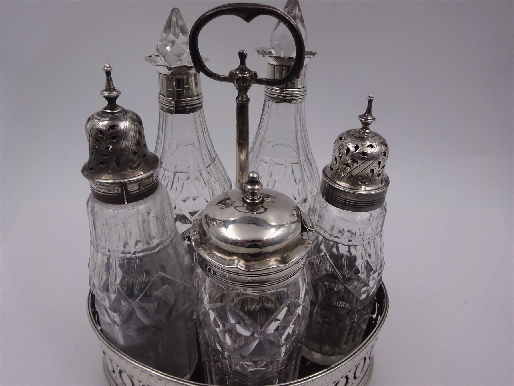 Late 18th century silver cruet stand, of oval form, with pierced sides upon four bun feet, hallmarked to handle Hester Bateman, all other hallmarks indistinct, together with five matched silver mounted cut glass cruet bottles, including some later Victorian examples, hallmarks predominantly indistinct, stand H20cm