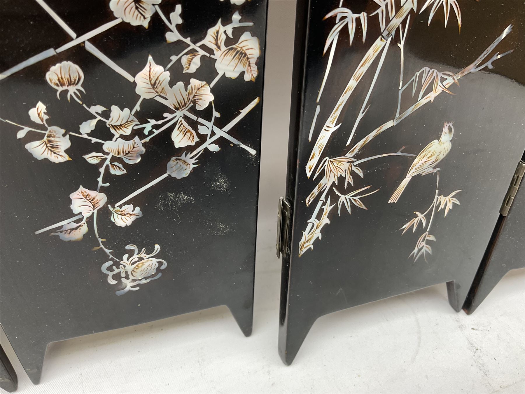  Late 19th / early 20th century Japanese lacquered table top cabinet, heavily decorated with mother of pearl inlay depicting blossoming branches, flowers and birds, the two hinged doors between longer drawers opening to reveal interior fitted with four short drawers, with lift up hinged canted lid, H28cm D9.5cm W23cm, together with mother of pearl inlaid miniature folding screen, dish decorated with walking figures with crimped edge, boxes decorated with flowers, birds and gilt etc