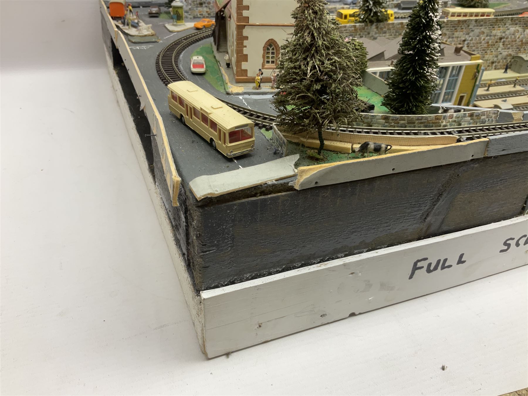 Table top 'N' gauge continental scenic layout as a split level town with various loops of track, station with numerous platforms, engine shed, assorted buildings, roads with motor vehicles and figures, tunnels, trees, river with bridge, tram depot etc 122 x 52cm