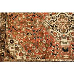 Persian Heriz-style rug, bold geometric octagonal medallion, rich red field with ivory spandrels, dark navy border, rosettes and vines; inner guards with repeating patterns 