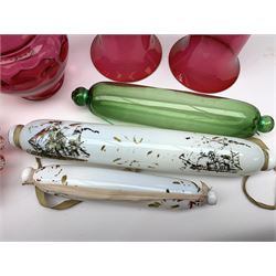 A group of 19th century glass, comprising two milk glass love token rolling pins, a green glass example, an opaque glass vase painted with birds and flowers, a green bottle, pair of cranberry glass bells with clear handles, cranberry pot and cover, and later cranberry jug. 