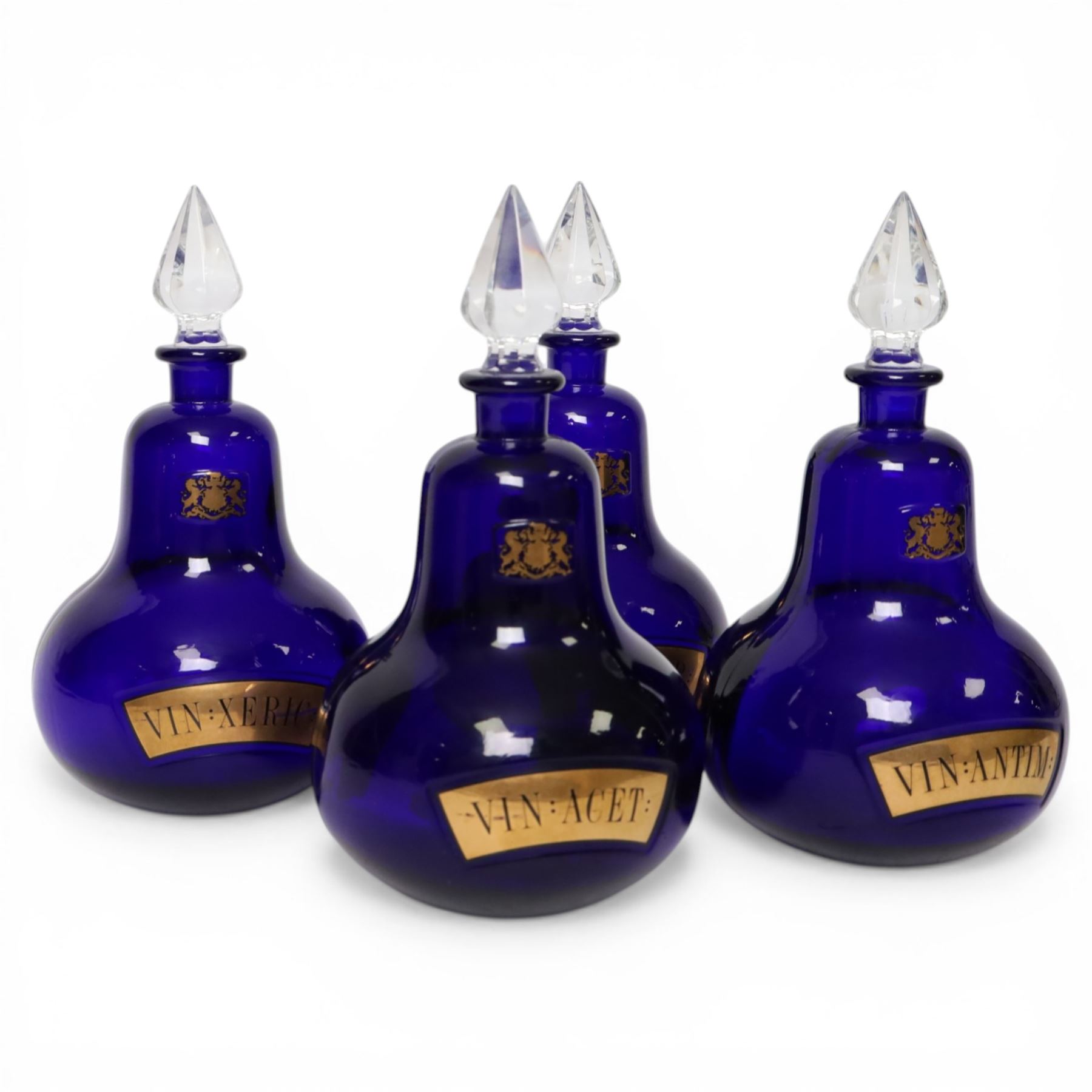 Set of four 20th century Royal Pharmaceutical Society blue glass bottles, of bellied form with clear cut glass spire stopper, each body bearing gilt label in Latin: VIN:ACET:, VIN:ANTIM:, VIN:XERIC:, and VIN:FERR:, and gilt Royal Pharmaceutical Society crest to neck, H25cm

Provenance: From the collection of the family of Peter Green, a practising pharmacist whose career spanned the mid to late 20th century. During his professional life he managed pharmacies in Yeovil, Somerset, and later Selles Chemist in Filey, North Yorkshire, before purchasing and running his own business, Peter Green Pharmacy, located in the Market Place, Malton. The bottles were displayed as part of the traditional shop fittings in both the Filey and Malton pharmacies and were retained as part of his collection.