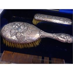 Four piece Edwardian silver mounted dressing table set, comprising hair brush, hand mirror, shoe horn and clothes brush, each embossed with cherubs, hallmarked Chester 1908, makers mark indistinct, together with a silver comb holder, hallmarked, contained within tooled leath, silk and velvet lined fitted case, 