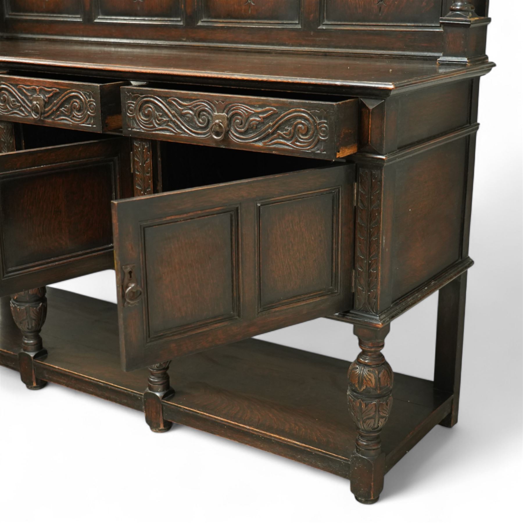 Early 20th century carved oak sideboard Jacobean style with panel back on cup and cover legs, the top section with carved panels and reeded moulding, three deep frieze drawers over triple panelled cupboard doors, raised on carved baluster legs joined by lower shelf