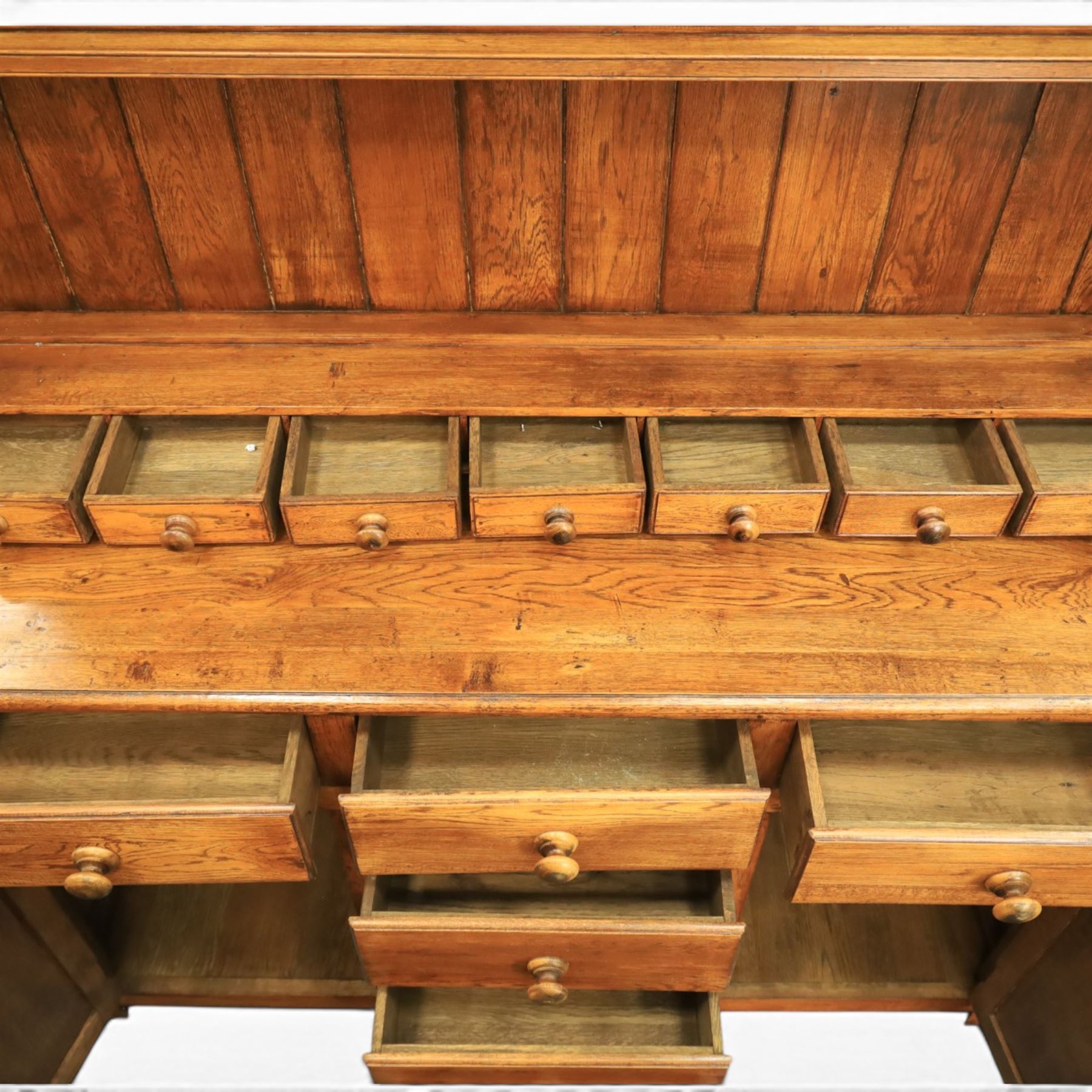 Traditional oak dresser with plate rack in the manner of Titchmarsh & Goodwin, plate rack with projecting cornice and shaped and pierced frieze, tongue and groove back three racks, over seven small spice drawers, the lower section with three short drawers, central bank three of drawers, fielded panelled sides and cupboard doors, raised on stile supports