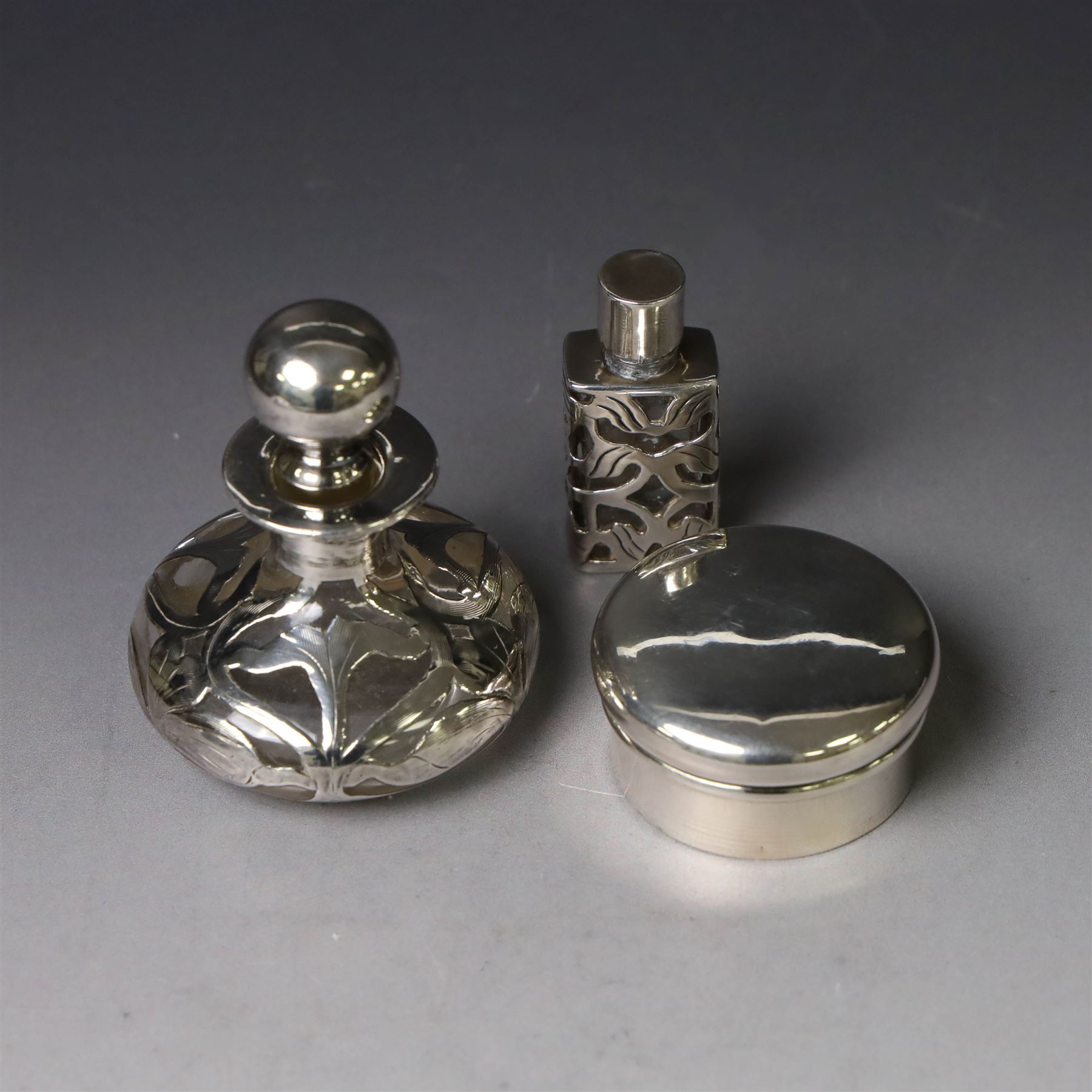Two early 20th century silver pill/patch boxes, together with two glass perfume bottles with silver overlay and stoppers, all stamped or hallmarked, smallest box D2cm, largest bottle H7cm