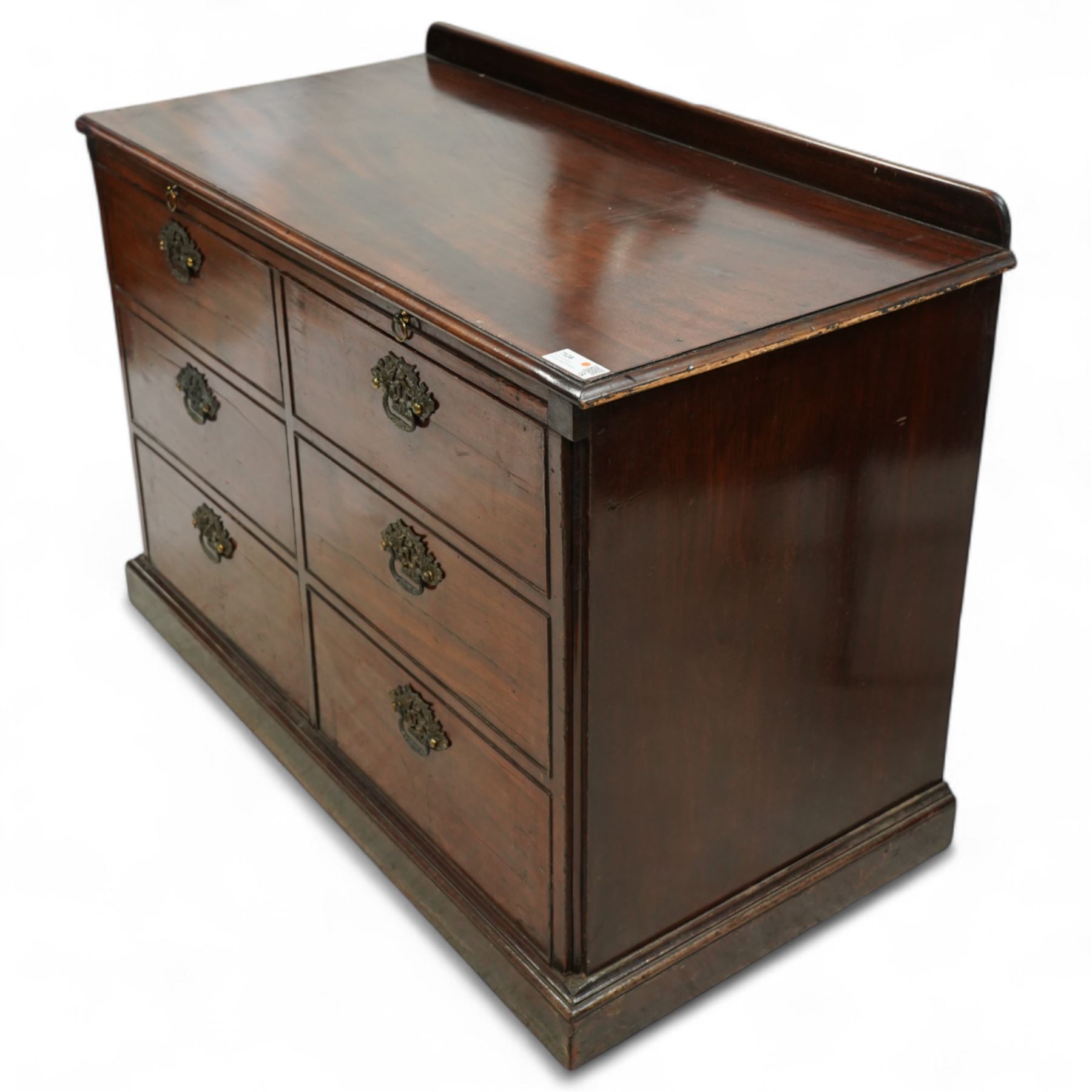 Early 20th century mahogany chest, rectangular top with raised gallery back with brushing slide on sliding tray, fitted with two cupboard doors behind six false drawer fronts, pierced brass handles on a plinth base