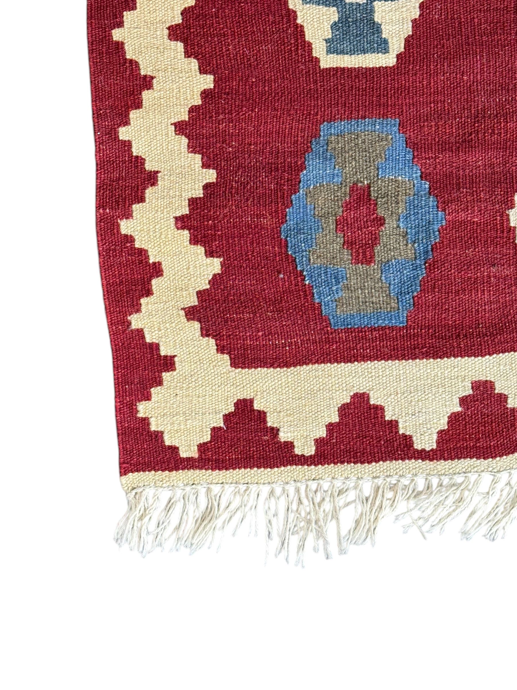Handwoven wool Kilim rug of rectangular form with cream fringe, the red ground decorated with repeated multicoloured hexagonal medallions within a cream stepped border